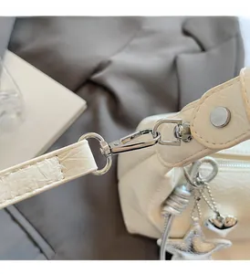 Vue macro d'un sac à main crème plissé avec boucles en métal argenté et breloques