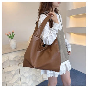 Close-up of a large brown tote bag in soft faux leather worn by a model in a warm setting