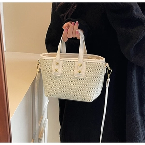 Detail of white woven bucket bag featuring gold rivets and detachable shoulder strap