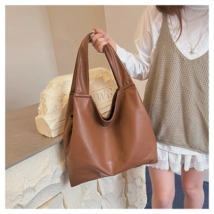 Brown leather tote bag featuring a spacious interior and minimalist handle on a model