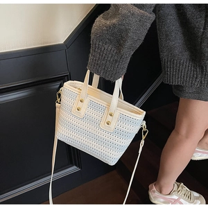Detail of woven bucket bag with beige leather handles and gold metal hardware