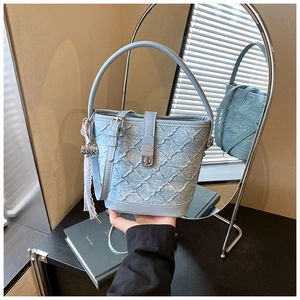 Dettaglio borsa a secchiello in denim celeste con trama trapuntata e nastro in pizzo