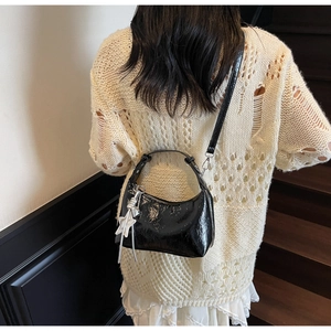 Détail d'un sac hobo en cuir verni noir avec pendentif étoile argentée porté par un mannequin