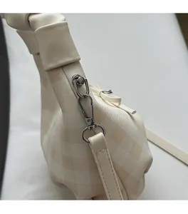 Dettaglio dei ganci in metallo argentato e del tessuto a scacchi crema della borsa a tracolla