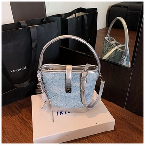 Détail d'un sac seau en denim bleu avec garniture argentée et boucle sur un coffret