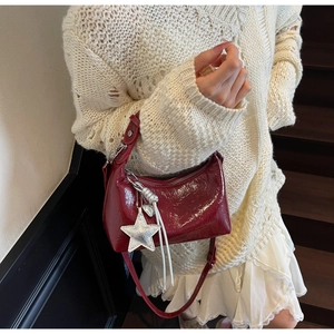 Detail of dark red glossy shoulder bag with silver star charm and wrinkled texture