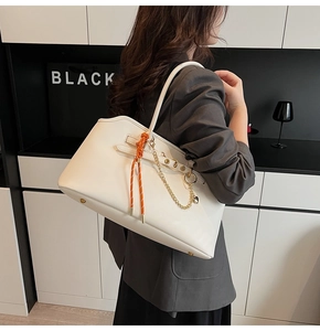 Detail of white leather tote bag featuring orange woven knot and gold chain accessory