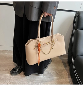 Dettaglio della borsa tote beige con catene dorate e corda arancione su giacca grigia