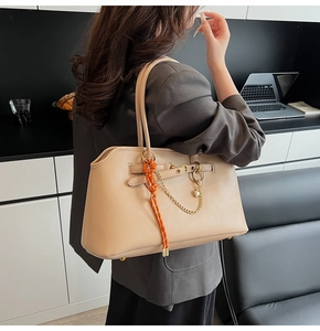 Close-up of beige shoulder bag with gold chain and orange woven charm in modern interior
