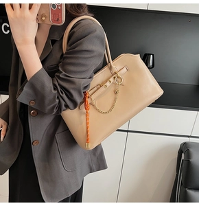 Dettaglio della borsa tote in pelle beige con catena dorata e ciondolo arancione a tracolla