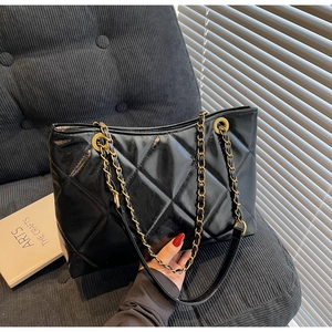 Dettaglio borsa shopper trapuntata nera con catena dorata su divano in velluto grigio