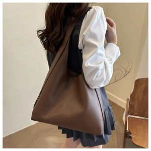 Detailed view of large brown leather tote bag worn by model in minimalist home setting
