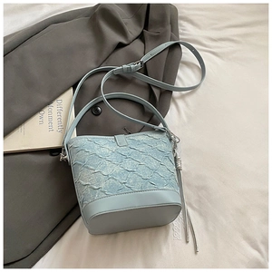 Sac seau bleu clair avec texture tissée et breloque à pompon argenté sur tissu blanc