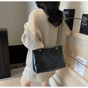 Dettaglio di una borsa a tracolla trapuntata nera con catena indossata da una modella