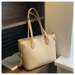Detail of beige litchi grain tote bag with metal studs and strap on a wooden shelf