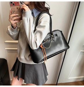 Dettaglio borsa tote in pelle nera con catena dorata e corda arancione