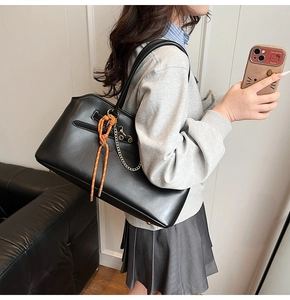 Detailed side view of a black leather tote bag with orange rope and gold chain detail