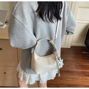Detail of cream patent leather half-moon bag with star pendant and fringe tassel
