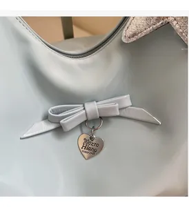 Detail of light blue faux leather bag featuring a tied bow and silver heart pendant