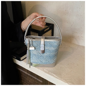 Détail d'un sac seau en denim bleu clair avec poignée en métal argenté et breloque