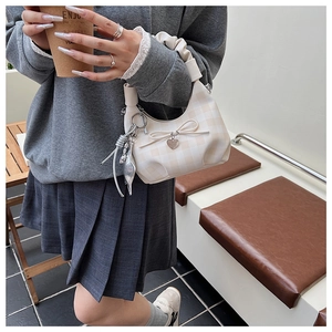Dettaglio borsa a quadretti beige con fiocco, ciondolo a cuore e manico arricciato