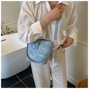 Détail du sac seau bleu clair texturé avec boucle argentée et breloque en dentelle