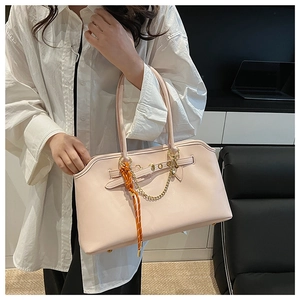 Dettaglio di una borsa tote beige con catena dorata e ciondolo con sciarpa di seta arancione