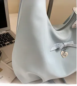 Detail of light blue satin tote bag with decorative bow and heart metal pendant charm