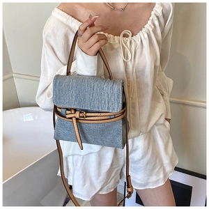 Detail of light blue denim tote with brown leather trim and golden metal hardware