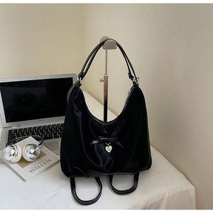 Detail of black satin backpack with ribbon bow and silver heart pendant in lifestyle setting