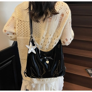 Detail of glossy black shoulder bag with heart pendant and silver star charm accessory