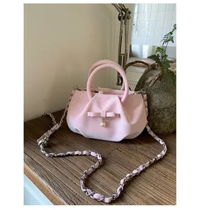 Detail of pink bow and pearl charm on a pleated leather handbag with chain strap