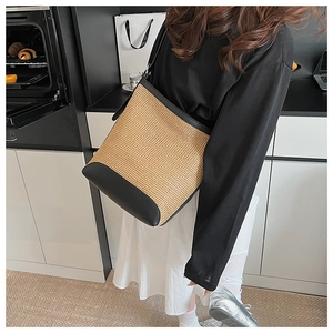 Detail of hand-woven straw bucket bag with black leather trim and adjustable strap