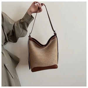 Detail view of woven bucket bag with brown leather trim and adjustable shoulder strap