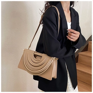 Détail du sac bandoulière beige clair plissé porté par un mannequin en costume noir