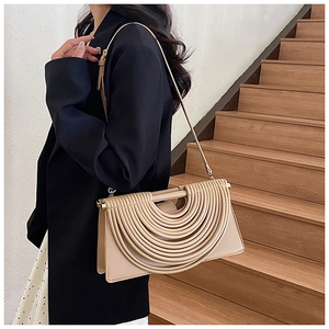 Détail du sac bandoulière beige plissé porté devant un escalier en bois