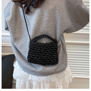 Détail d'un sac à main noir en cuir tressé porté par un mannequin dans un salon