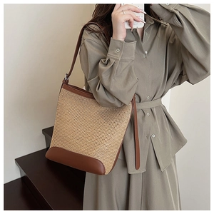 Detail of woven straw shoulder bag with brown leather trim styled on a model's shoulder