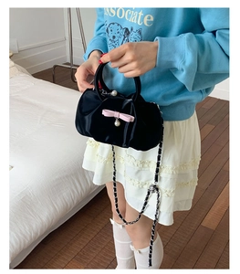 Close-up of black velvet handbag with pink bow, pearl pendant, and chain strap detail