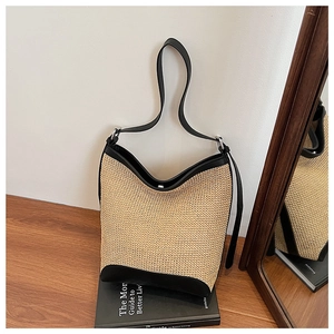 Detail of woven straw shoulder bag with black leather trim and strap on a book