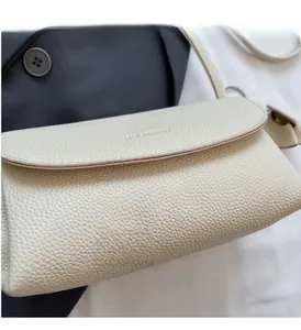 Detail of creamy white litchi pattern leather bag with embossed logo on the flap