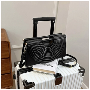 Détail d'un sac à main noir en cuir avec plis semi-circulaires sur une valise blanche