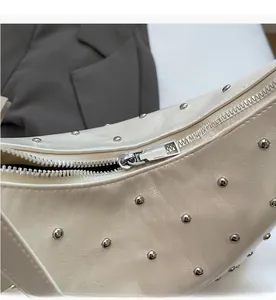 Detailed macro view of silver metal zipper and rivet studs on beige leather shoulder bag