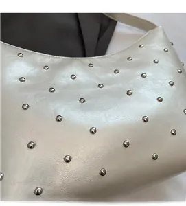 Detailed close-up of white leather bag with shiny silver stud accents and fine texture