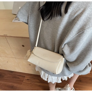 Detail of a creamy beige lychee grain leather crossbody bag with a silver cat charm