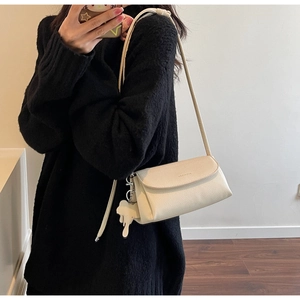 Detail of creamy white litchi leather crossbody bag with elephant charm and WEARME logo