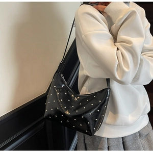 Detail of glossy black moon bag with silver rivets and sleek shoulder strap worn by model