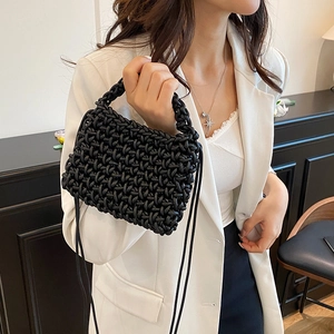 Sac tressé noir fait main pour femme porté avec un costume blanc dans un décor épuré