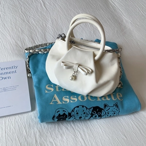 White pleated bow handbag with pearl pendant and chain strap in casual setting