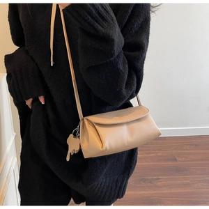 Detail of beige litchi grain leather crossbody bag with cute elephant charm accessory